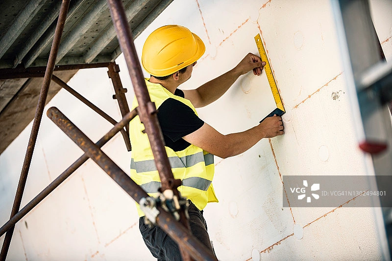 Construction Worker Installing EPS Foam Insulation Board on Building Wall with Level Tool